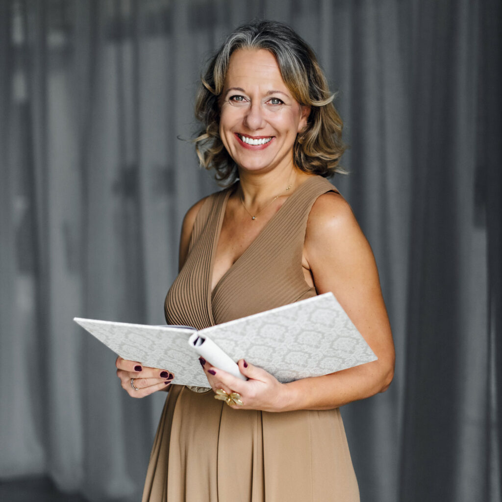 Eine Geleitgeberin hält lachend ein großes weißes Buch in den Händen.