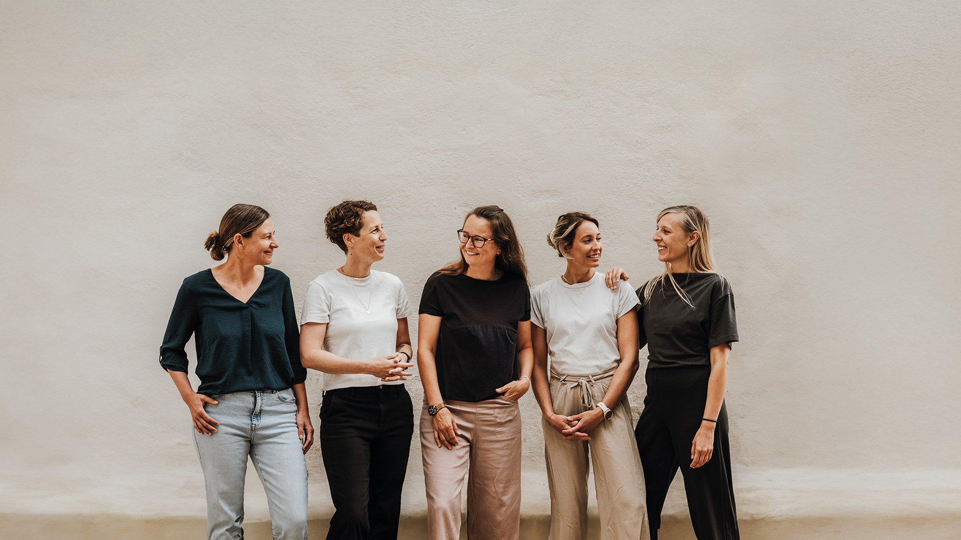 Femunity: Fünf Frauen stehen lächelnd nebeneinander vor einer hellen Wand.“