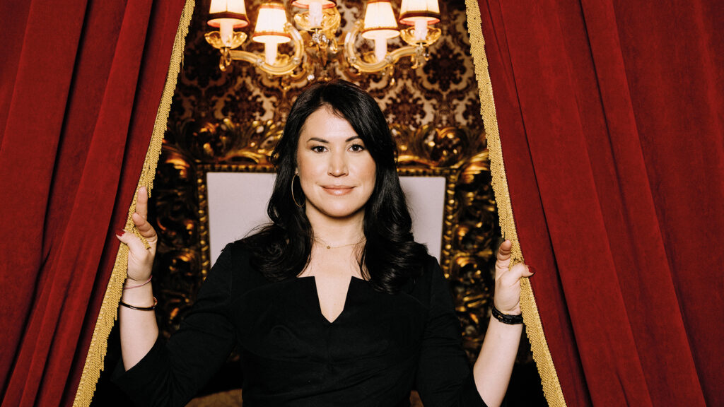 Vea Kaiser: Frau steht zwischen roten Samtvorhängen und blickt in die Kamera.