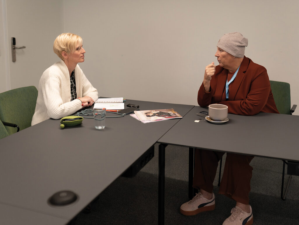 Zwei Personen sitzen einander in einem Besprechungsraum gegenüber und führen ein Gespräch.