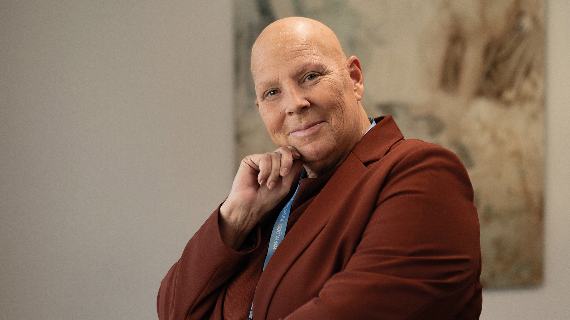 Porträt einer lächelnden Person im braunen Blazer vor hellem Hintergrund.