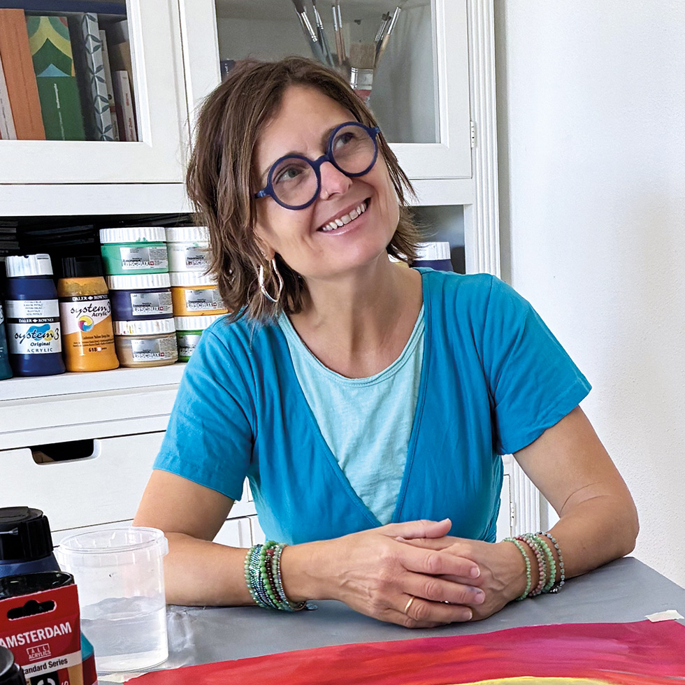 Frau mit Brille sitzt an einem Tisch und lächelt hinauf