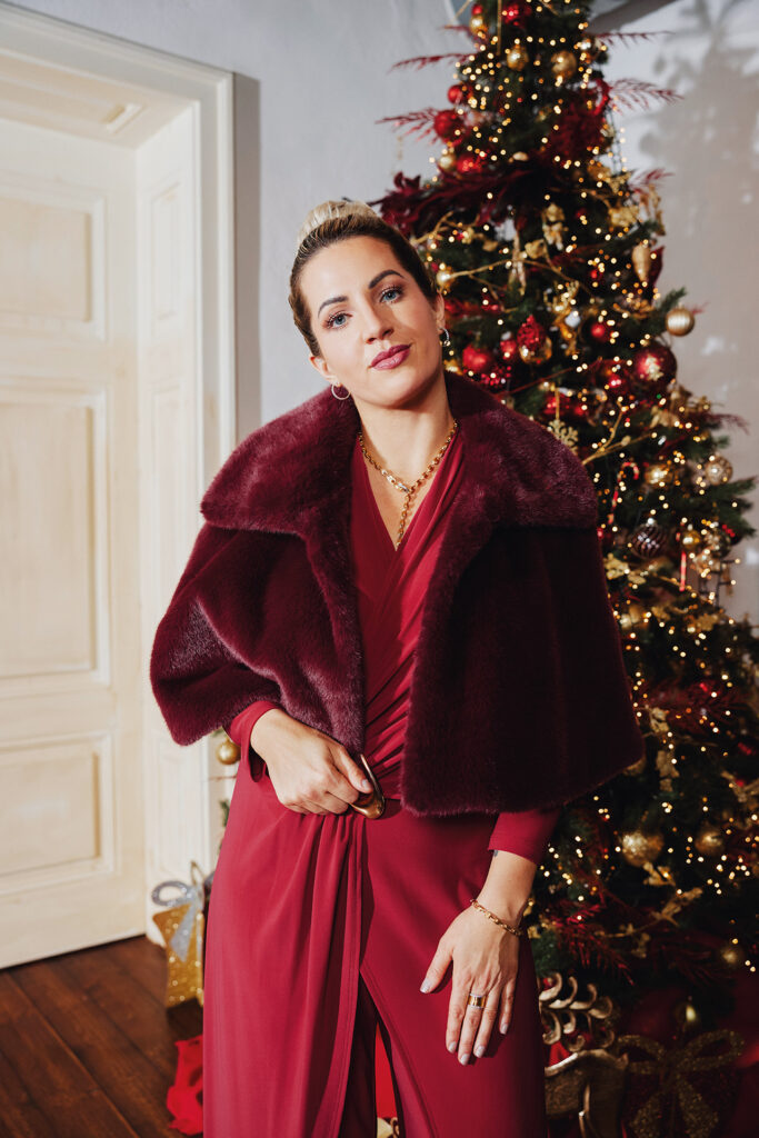 Frau in rotem Abendkleid steht vor weihnachtlich geschmücktem Weihnachtsbaum.