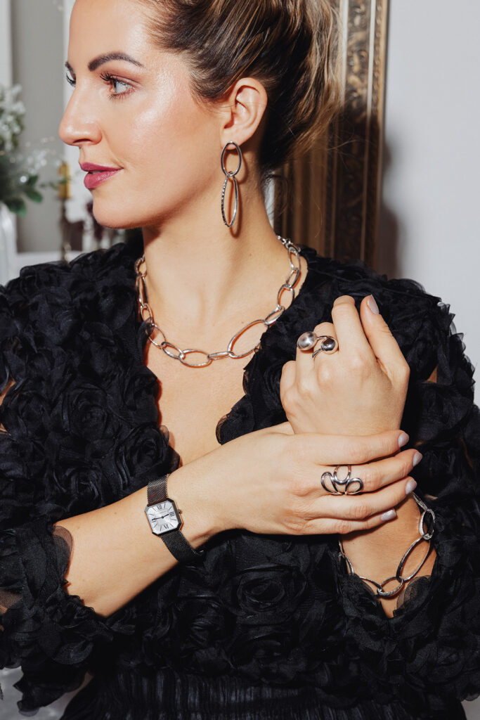 Nahaufnahme einer Frau mit silbernem Schmuck und Uhr, in schwarzem Outfit.