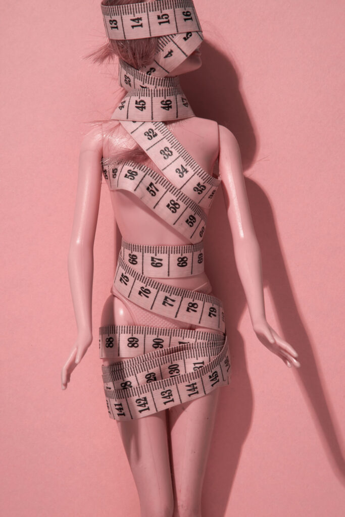 Konfektionsgrößen: Rosa Barbiepuppe eingewickelt in Maßband.