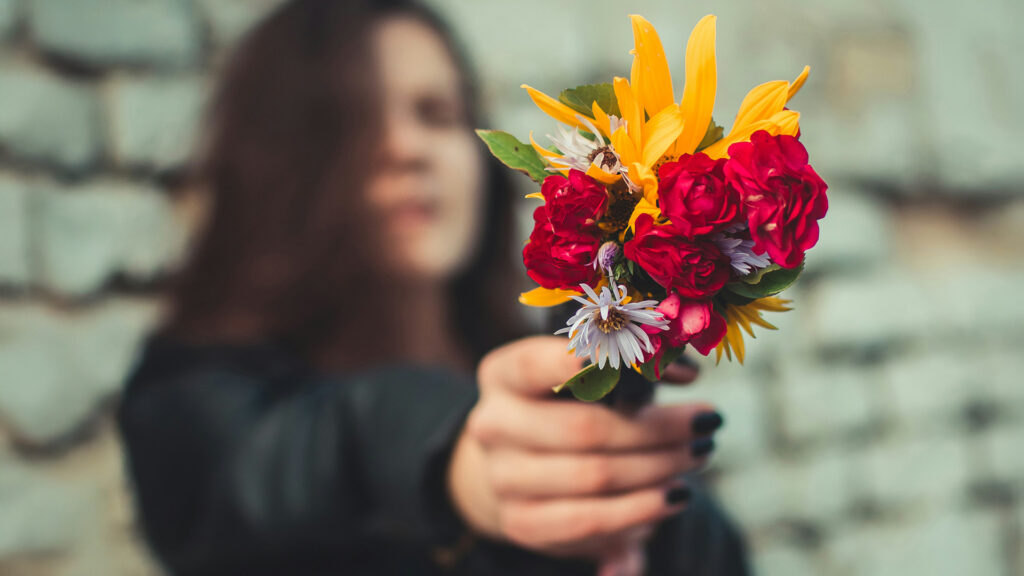 Valentinstag: Frau hält Blumenstrauß in die Kamera, wobei sie unscharf ist