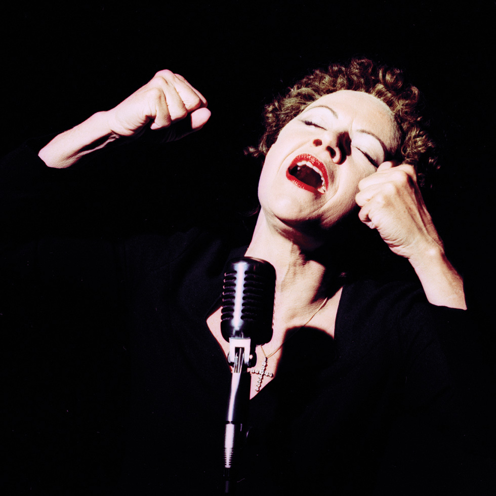 Maria Bill: Sängerin mit Mikrofon in emotionaler Gesangspose auf dunkler Bühne.