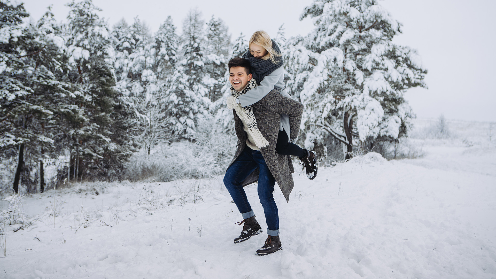 Bewegung im Winter: Mann trägt lachende Frau huckepack in einer Winterlandschaft