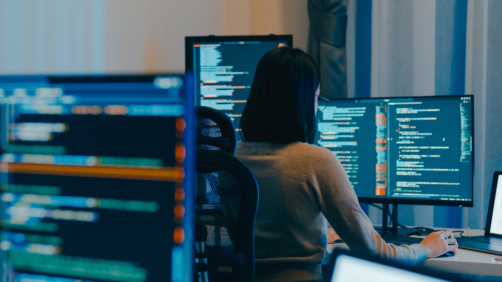 IT: Entwicklerin arbeitet an mehreren Bildschirmen mit Code.“