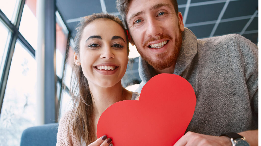 Valentinstag: Junges Pärchen mit rotem Papierherz in den Händen