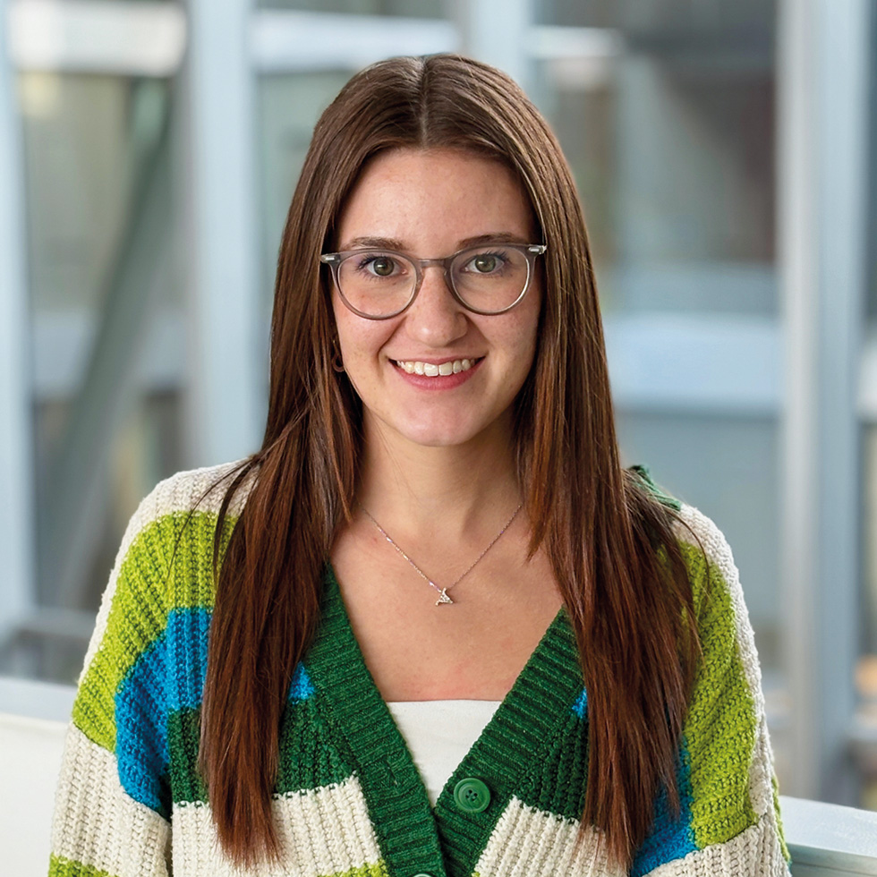 Lena Sagmeister: Portrait einer jungen Frau mit langen rot-braunen Haaren und brauner Brille in einer grün-weiß-türkisen Strickweste
