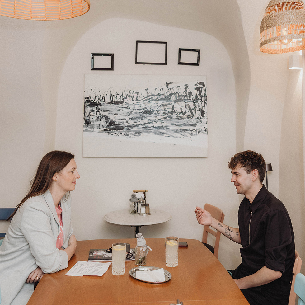 Michael Steiger im Interview mit einer Frau – beide an einem Tisch sitzend mit Mineral-Zitron darauf