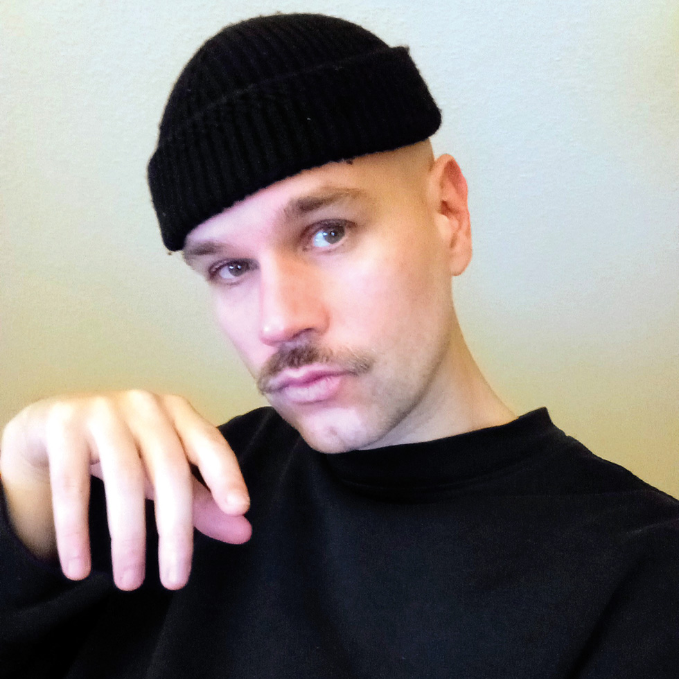 Detoxmasculinity: Portrait eines Mannes mit Mütze und Schnurrbart in ruhiger, reflektierter Pose