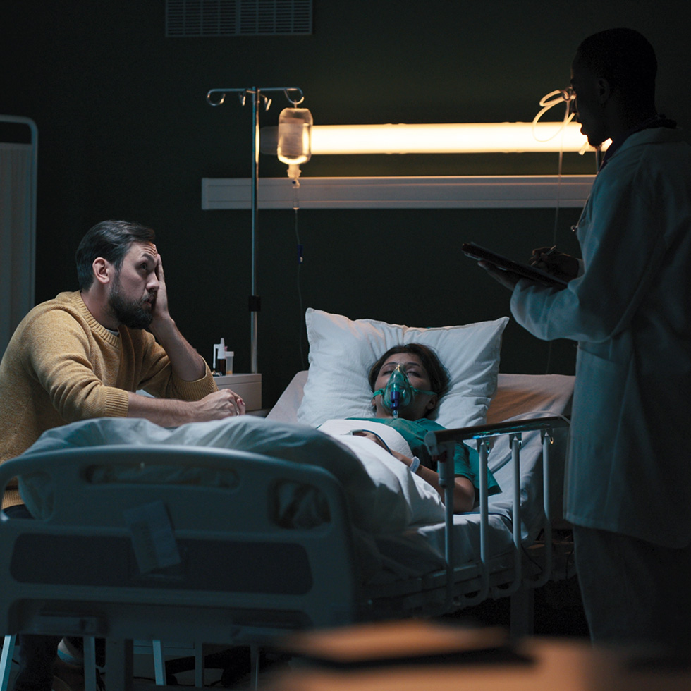 Letzte Hilfe: Patientin liegt im Krankenhausbett, Angehöriger und Arzt stehen daneben