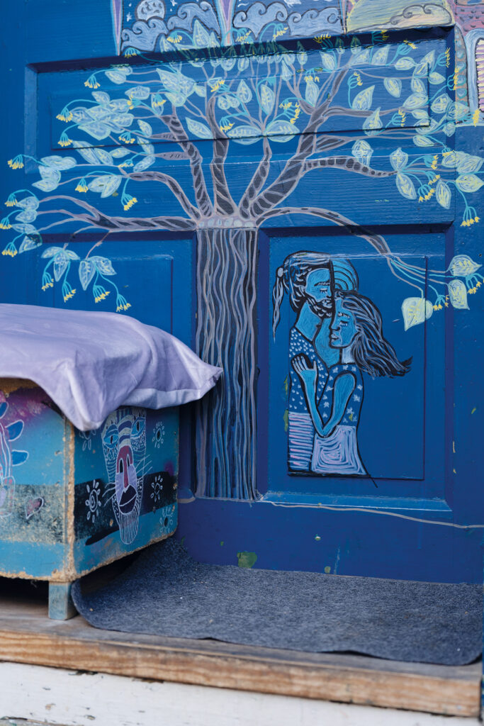 Blau bemalte Wand mit Baum- und Figurenmotiv neben einem Kissen