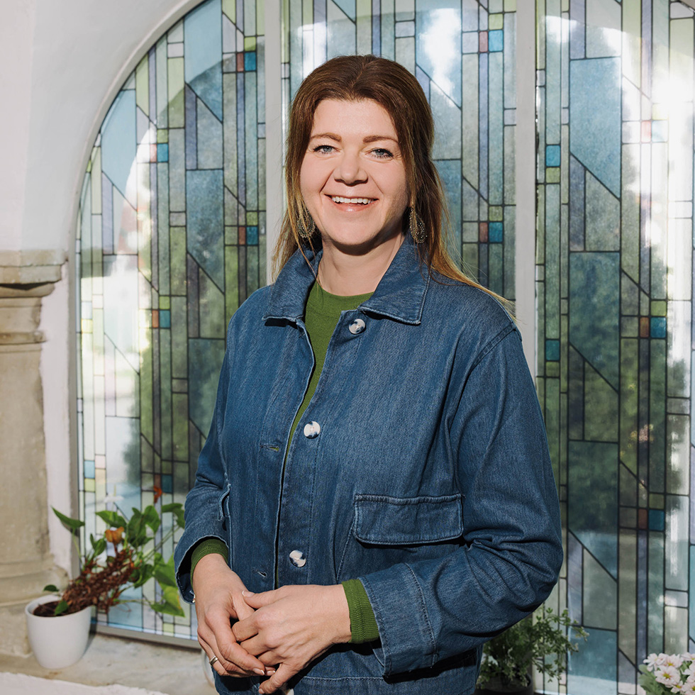 Passion: Frau lächelt vor einem großen Fenster mit Glasornamenten