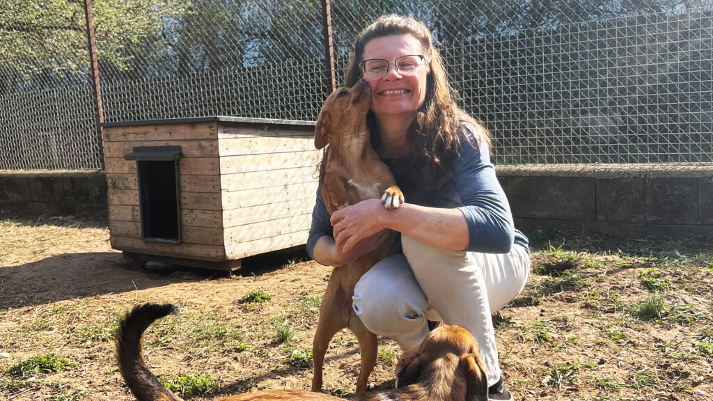 Tierheim: Frau kniet und wird von Hund im Gehege umarmt