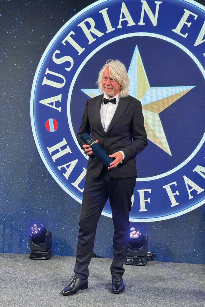 Ewald Tatar im schwarzen Anzug steht auf einer Bühne bei einer Preisverleihung vor einem „Austrian Hall of Fame“-Hintergrund und hält eine Auszeichnung.