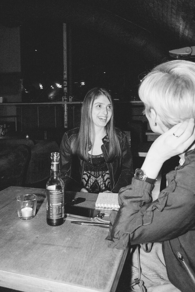Zwei Frauen sitzen an einem Tisch in einer Bar, lachen und unterhalten sich bei Getränken.