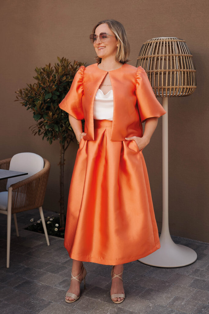 Mutter-Tochter-Shooting: Eine Frau trägt ein elegantes orangefarbenes Outfit und posiert selbstbewusst im Freien.