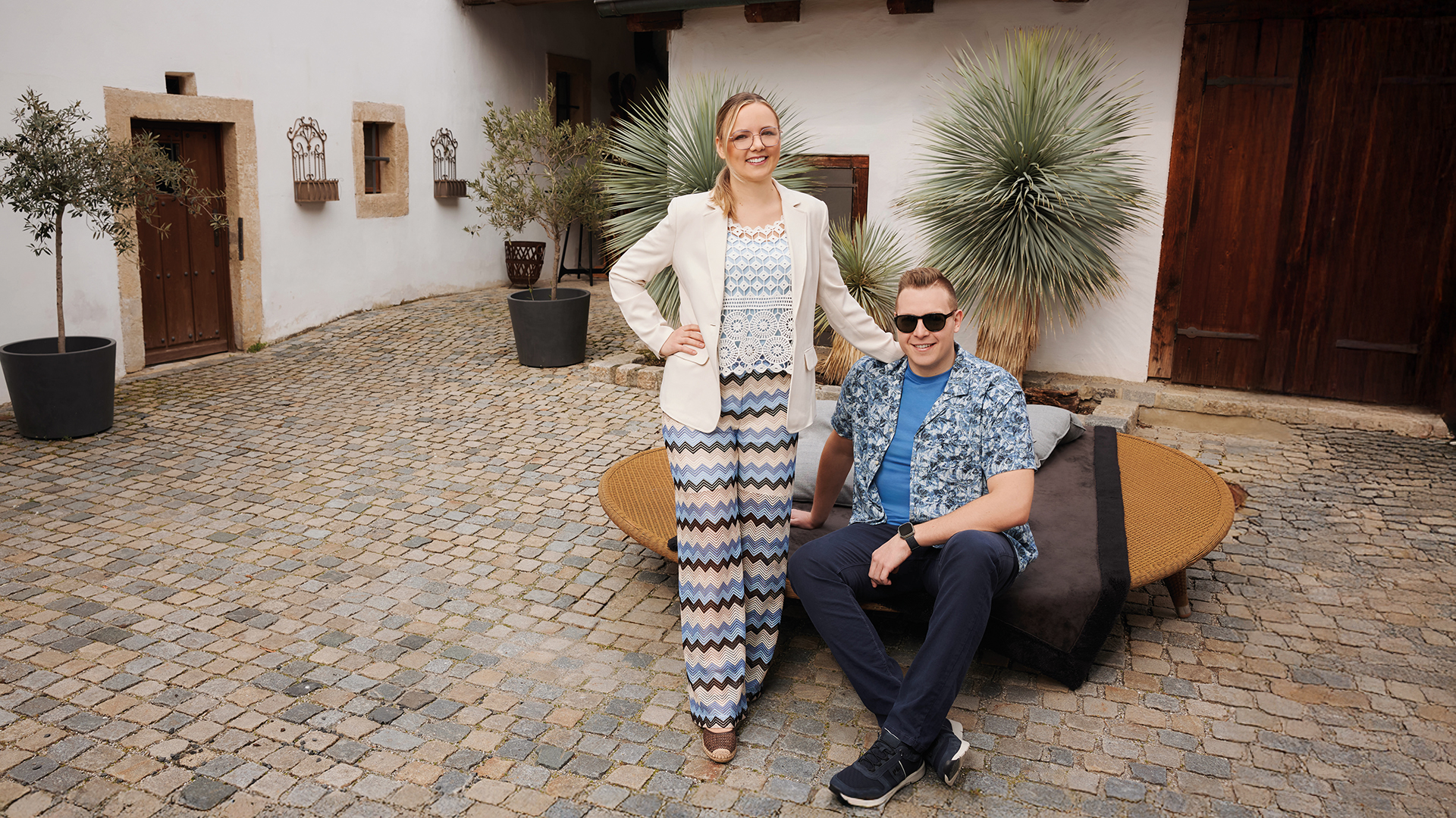 Mode: Frau und Mann posieren gemeinsam in Innenhof vor rustikalem Gebäude