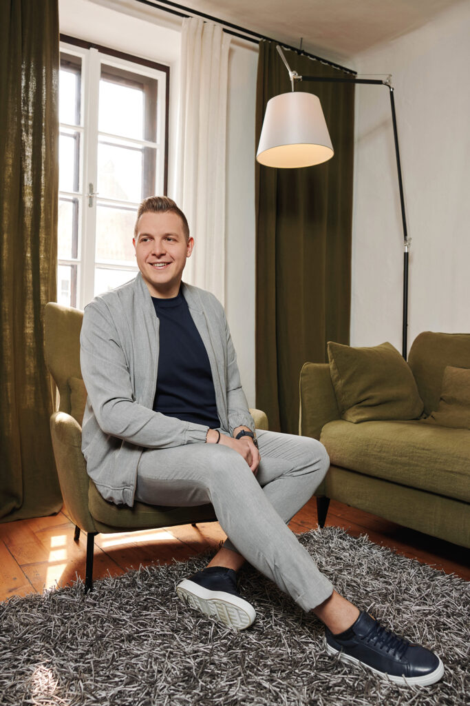 Mode: Mann sitzt in modernem Wohnzimmer auf Sessel neben Fenster und Stehlampe