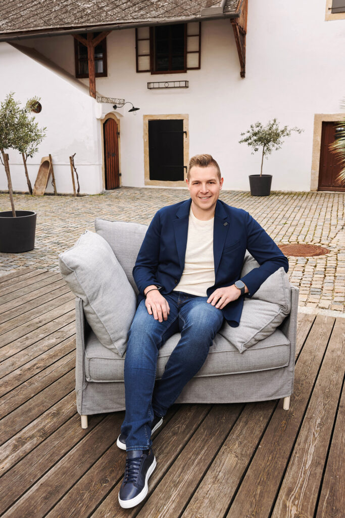 Mode: Mann sitzt auf Sessel im Innenhof vor weißem Gebäude mit Holztüren