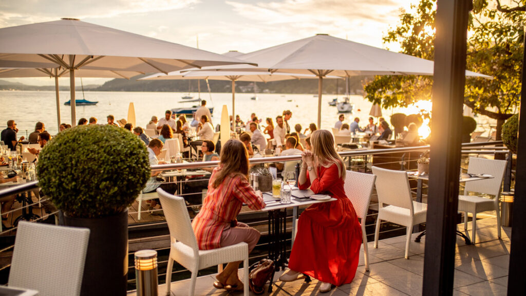 Events Österreich: Gäste genießen Essen und Getränke auf einer Terrasse am See bei Sonnenuntergang – kulinarisches Event in Österreich.
