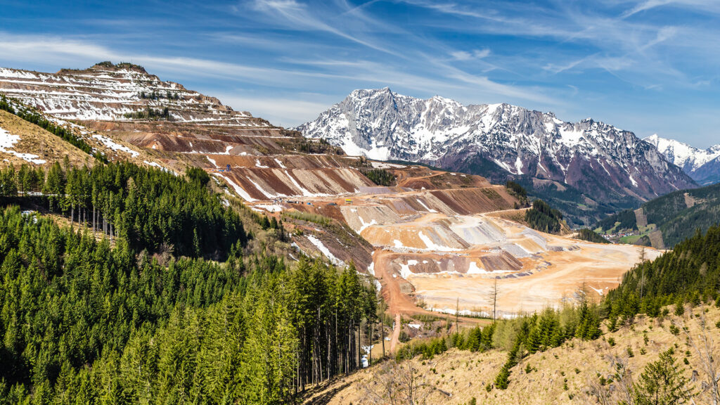 Events Österreich: Tagebau am Erzberg mit terrassierten Abbauflächen vor alpiner Berglandschaft – Industrielandschaft in Österreich.