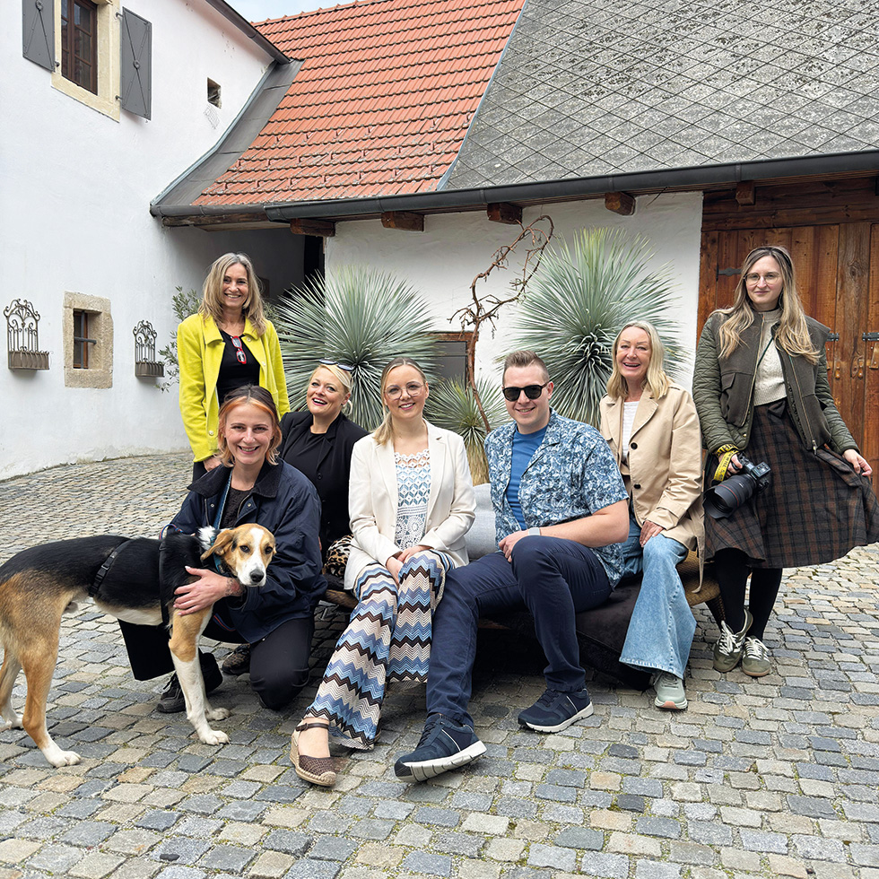 Gruppe von Menschen mit Hund sitzt und steht in Innenhof vor Hausfassade