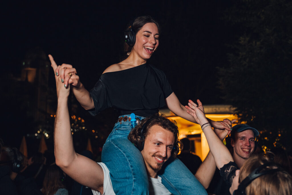 Was ist los: Besucher feiern bei einer Silent Disco unter freiem Himmel mit Kopfhörern und Festivalstimmung.