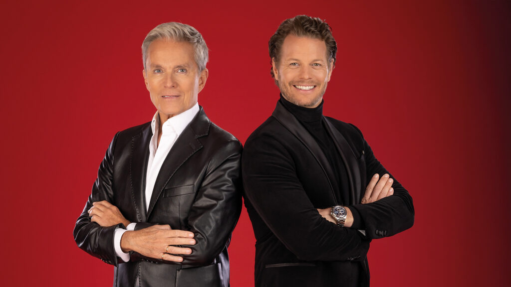 Ein Käfig voller Narren: Alfons Haider und Mark Seibert im eleganten Studio-Porträt vor rotem Hintergrund.