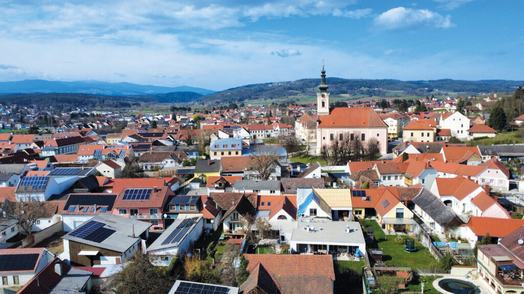 Pinkafeld aus der Vogelperspektive: Blick über die Dächer der Stadt mit Kirche und sanften Hügeln im Hintergrund.