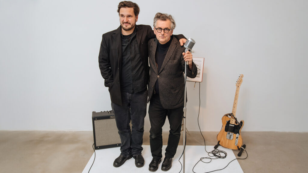 Events Juni: Zwei Männer stehen gemeinsam vor einem Mikrofon, daneben Verstärker und E-Gitarre in einer reduzierten Studio-Szene.