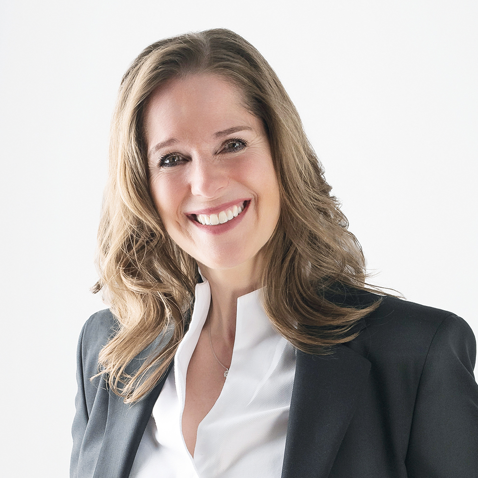 Hack your Health: Businessporträt einer lächelnden Frau in schwarzem Blazer und weißer Bluse vor hellem Hintergrund.