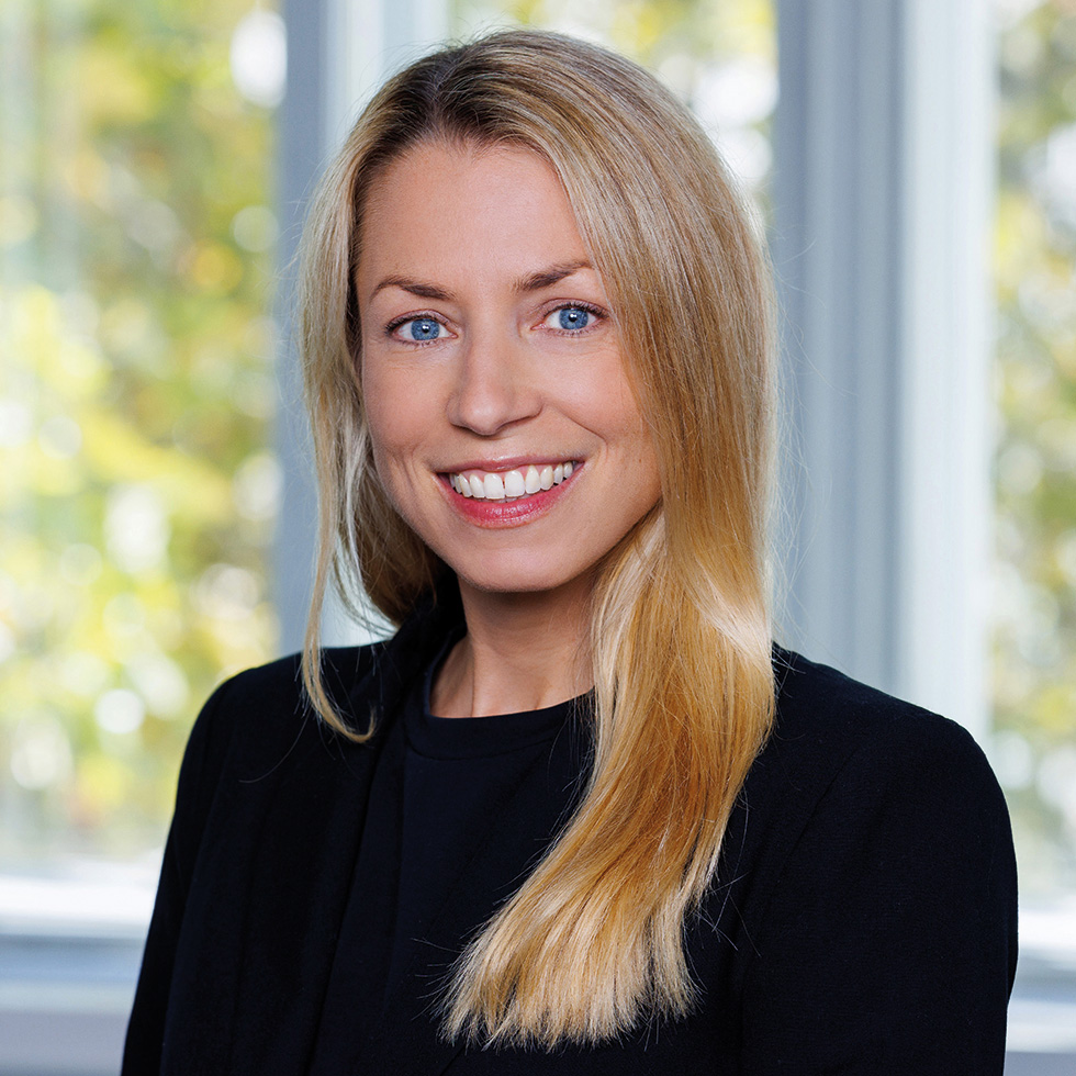 Hack your Health: Businessporträt einer blonden Frau in schwarzem Blazer vor hellem Fensterhintergrund.