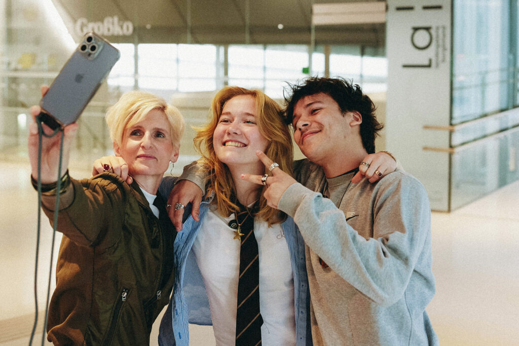 Churro64 und Luisa Schweig machen gemeinsam mit einer dritten Frau ein Selfie in moderner Architekturkulisse.