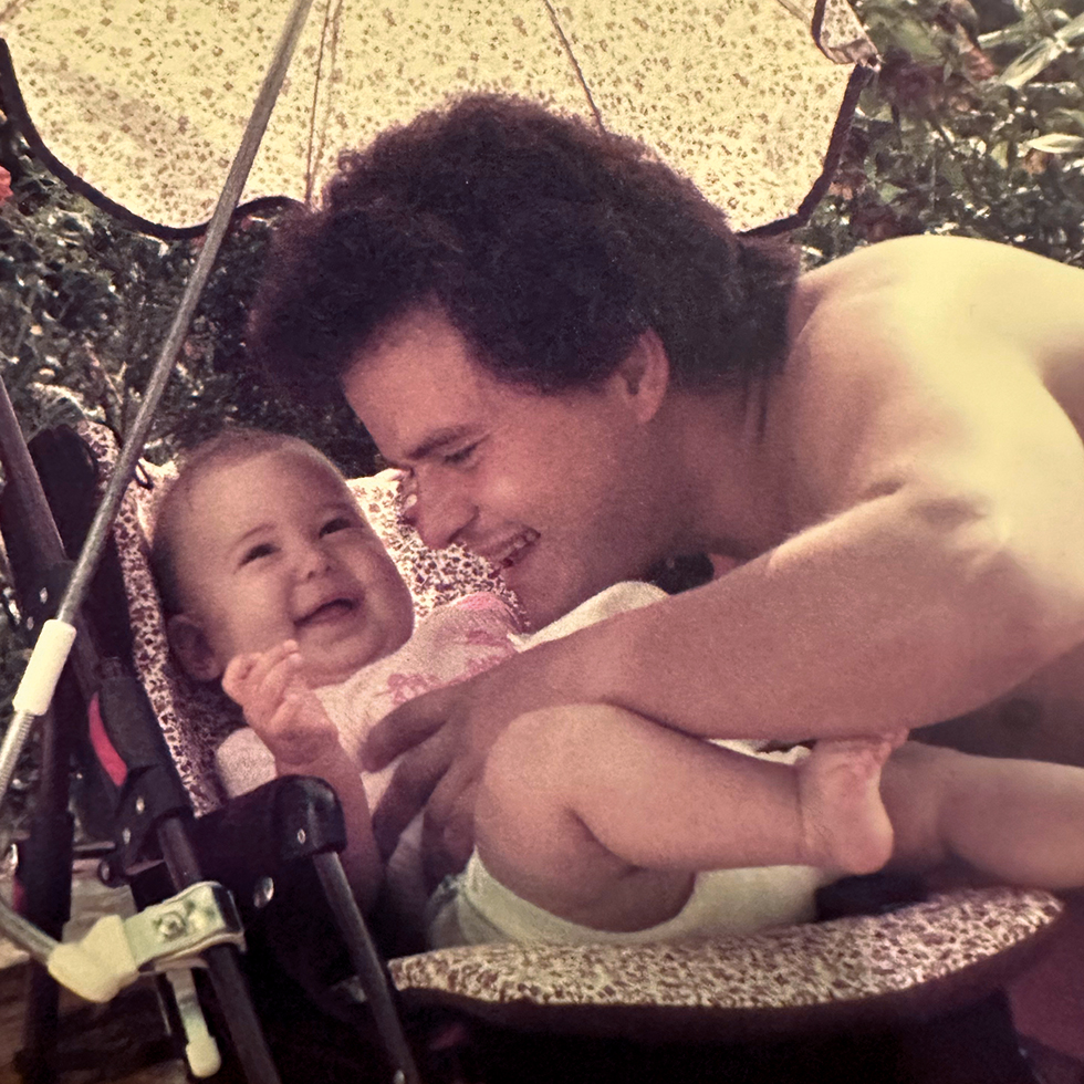Vater spielt liebevoll mit seinem Baby im Kinderwagen bei einem sommerlichen Familienmoment zum Vatertag.