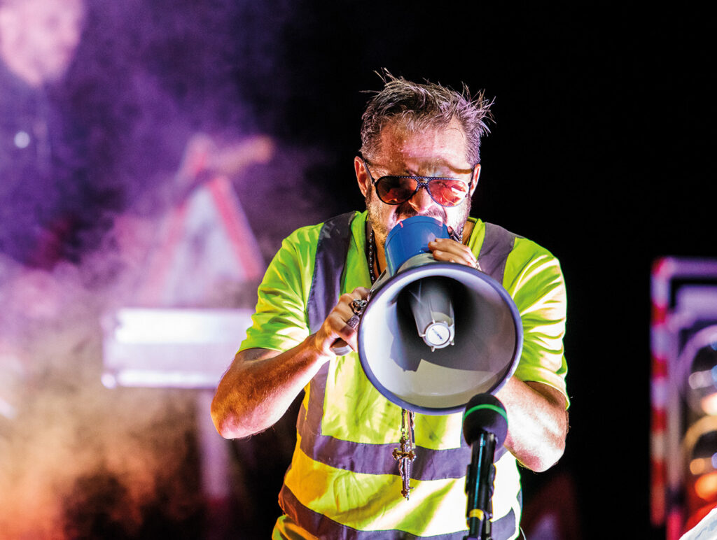 Kunst: Künstler performt mit Megafon und auffälligem Bühnenoutfit bei einer energiegeladenen Live-Inszenierung.
