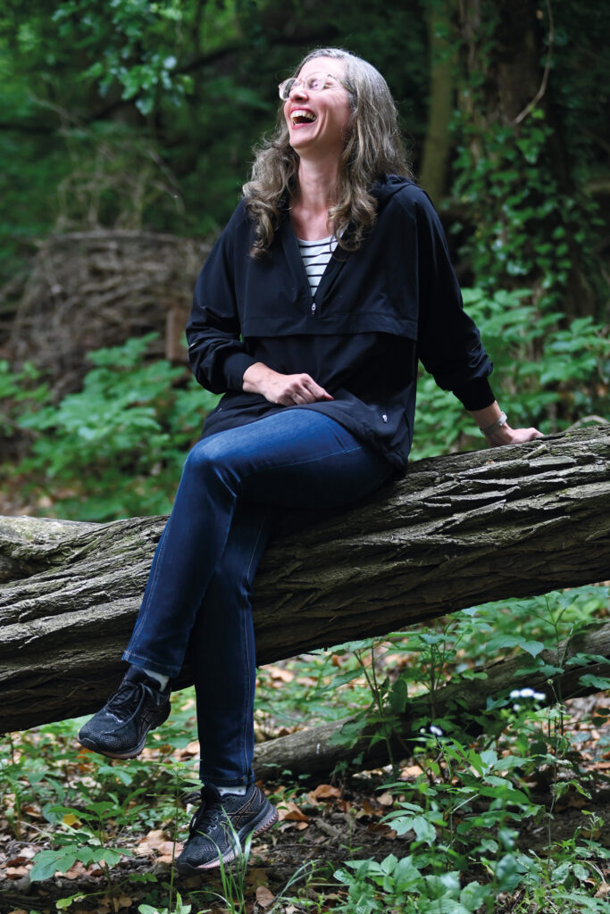 Landeshauptmann-Stellvertreterin Anja Haider-Wallner sitzt lachend auf einem Baumstamm im Wald.