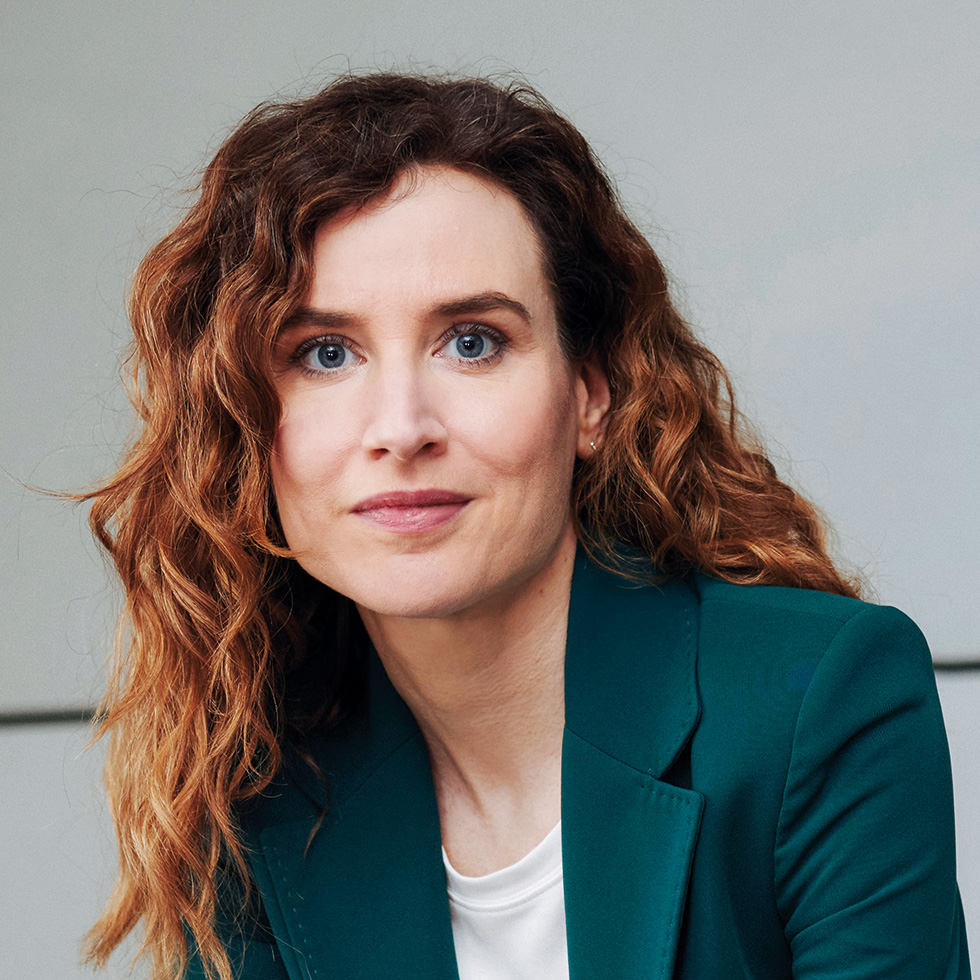 Top 100: Porträt einer Frau mit lockigem Haar und grünem Blazer – ausgezeichnet für ihren Beitrag in Wirtschaft, Wissenschaft oder Gesellschaft.