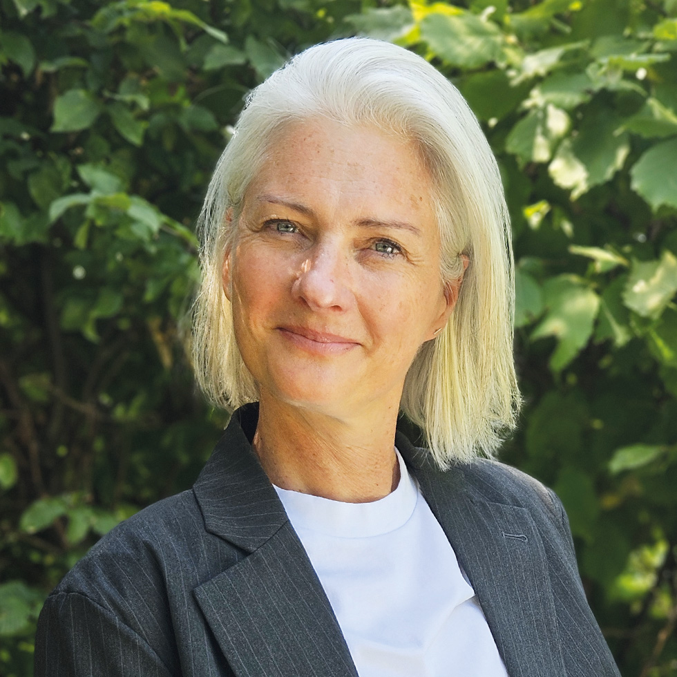 Top 100: Porträt einer Frau mit silbernem Haar im Business-Outfit vor grünem Hintergrund.