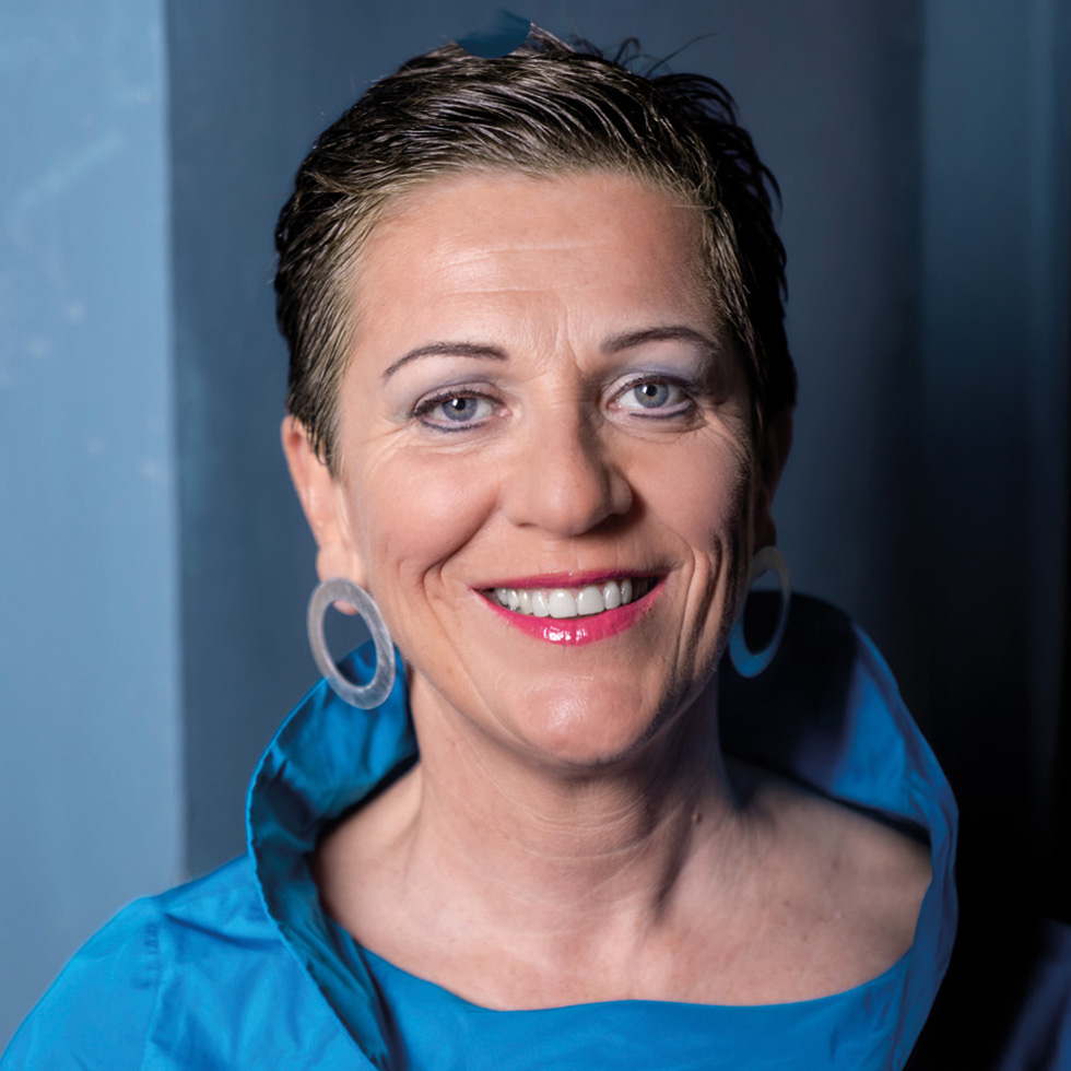 Porträt einer Frau mit kurzem Haar und blauem Outfit – eine der prägendsten Persönlichkeiten der Top 100.
