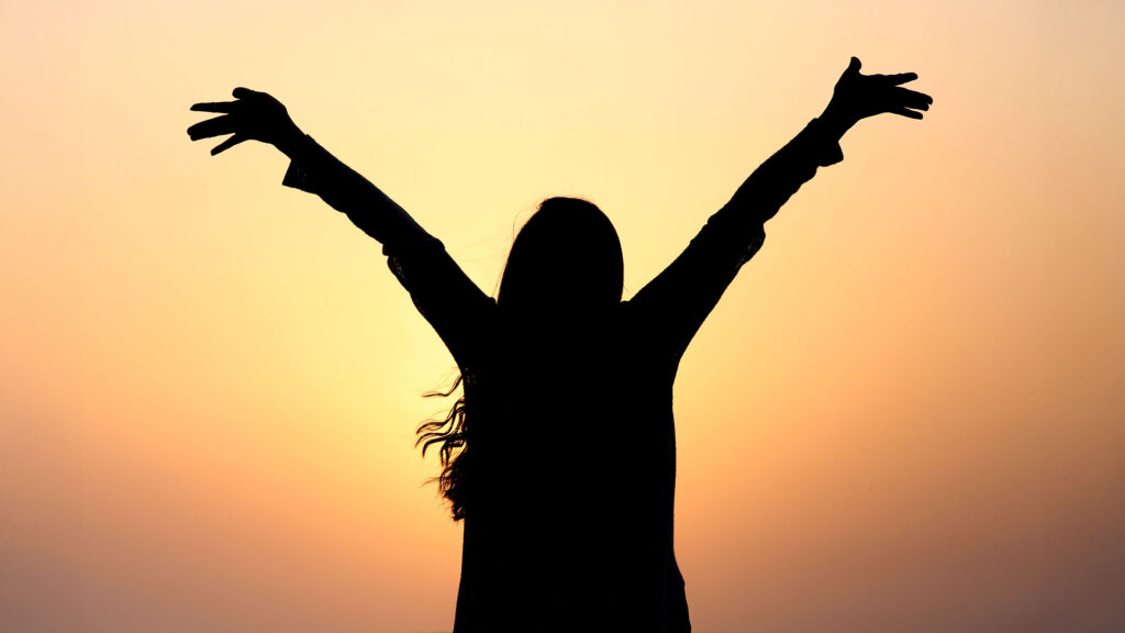 Top 100: Silhouette einer Frau mit ausgebreiteten Armen vor einem Sonnenuntergang – Symbol für Erfolg, Inspiration und die Top 100 Persönlichkeiten des Jahres.