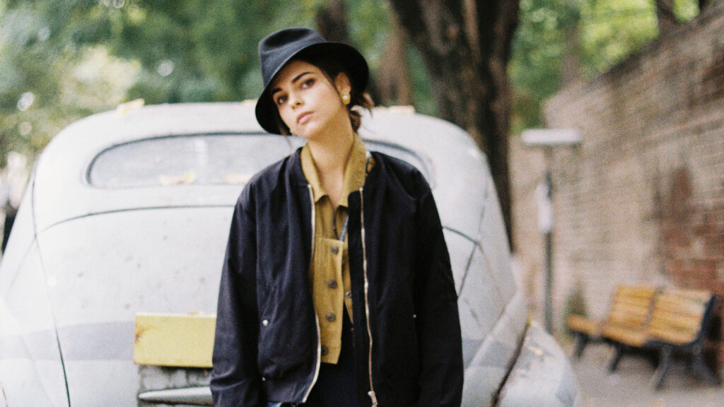 Kulturtipps im September: Junge Frau mit Hut vor einem Oldtimer in stimmungsvoller Szene.