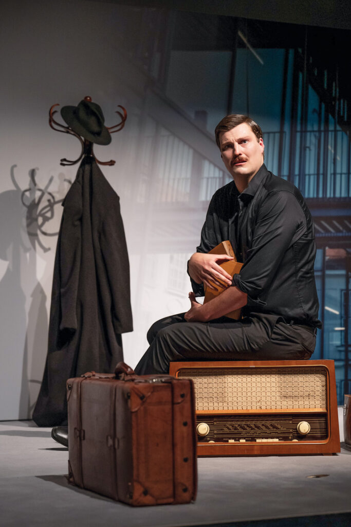 Theater im September: Schauspieler auf der Bühne mit altem Radio und Reisekoffer.