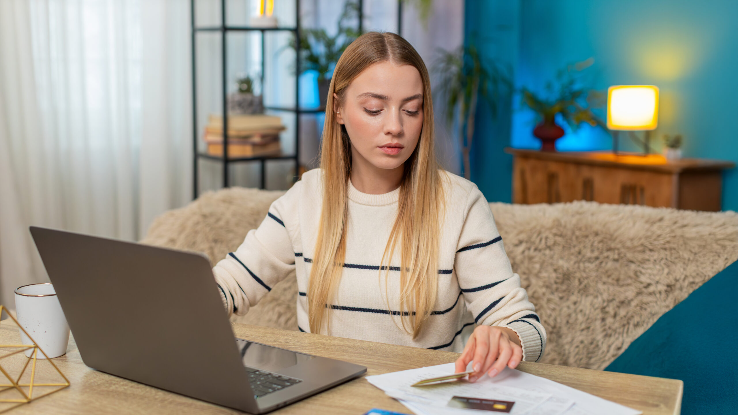 Female Finance: Frau organisiert selbstständig ihre Finanzen und prüft Bankkonto und Unterlagen am Laptop.