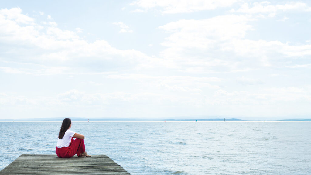 Nincshof am Neusiedler See: Frau sitzt auf einem Holzsteg und blickt über den See.