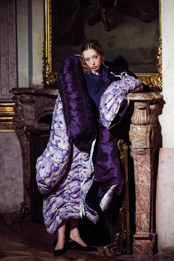 Selina Heindl bei einem Designershooting in einem extravaganten violetten Outfit vor historischer Kulisse.