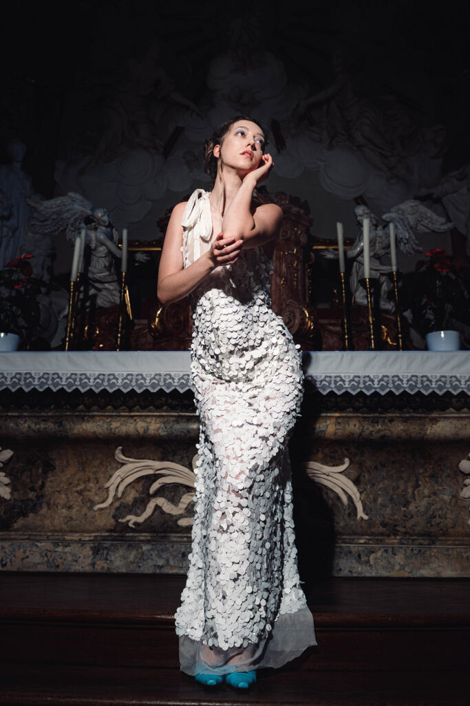Selina Heindl bei einem Designershooting im eleganten weißen Paillettenkleid vor einem historischen Altar.